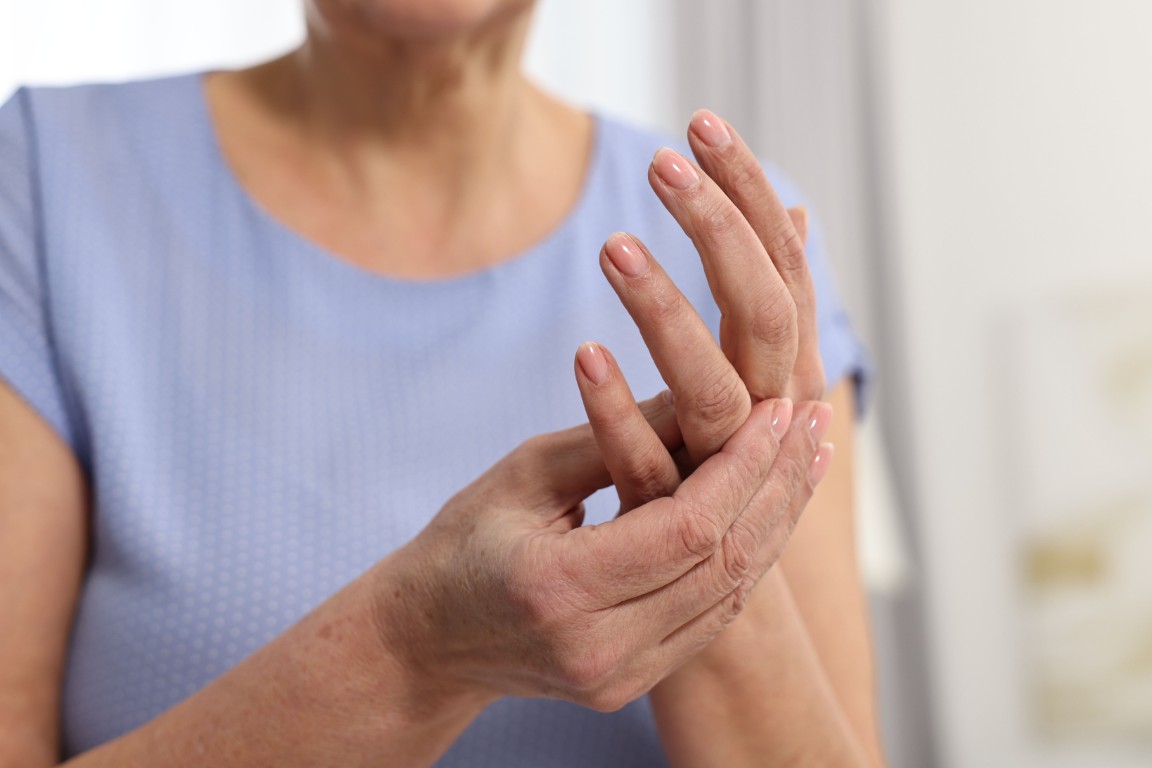 An elderly woman holds her hand to massage pain from arthritis